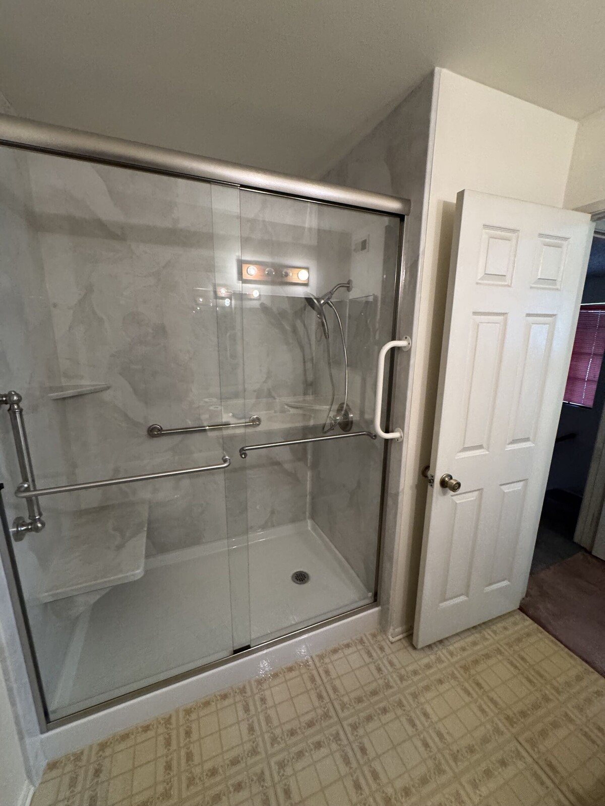 A modern, glass-enclosed walk-in shower featuring safety grab bars and a built-in seat highlights the practical and accessible results of a professional bathroom remodeling project.